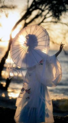 a woman holding an umbrella standing next to the ocean