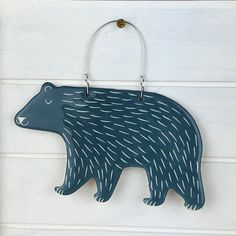 a blue bear ornament hanging on a white wall with a metal hook in the shape of a bear