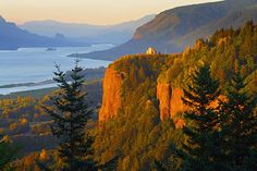 the sun is setting over some mountains and trees with water in the backround