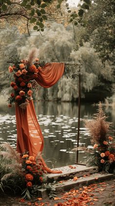 an outdoor ceremony setup with flowers and orange draping on the side of the aisle