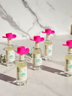 six bottles of hand sanitizers on a marble countertop with pink caps and handles