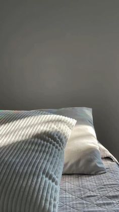 a bed with two pillows on top of it next to a gray wall and window