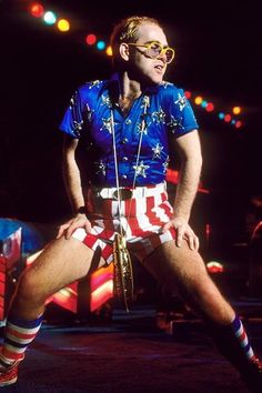 a man in patriotic shorts and sunglasses sitting on stage with an american flag shirt over his body