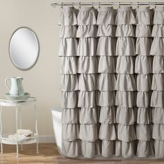 a white shower curtain with ruffles on the bottom and an oval mirror above it