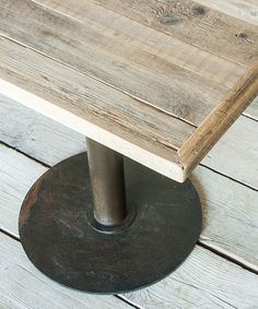 a wooden table sitting on top of a wooden floor next to a metal pole and potted plant