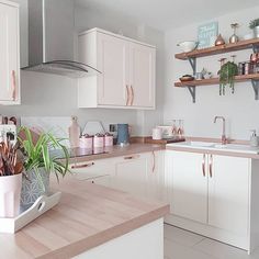 a kitchen filled with lots of white cabinets and wooden counter tops next to a potted plant