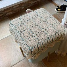 a crocheted tablecloth sits on top of a stool in front of a window