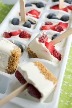 popsicles with berries, blueberries and strawberries are on a white tray lined with green tablecloth