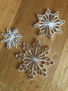 three white paper snowflakes sitting on top of a wooden table next to each other