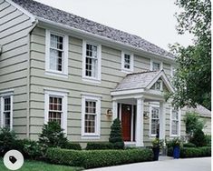 a house with white trim and two story windows on the front, surrounded by trimmed hedges