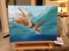 a painting of a sea turtle in the ocean on an easel next to a couch