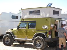 a man standing next to a green jeep with a camper on it's back