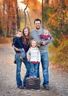 a family posing for a photo in the woods with fall foliage and trees behind them