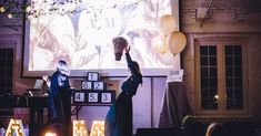 two people standing on stage in front of a projector screen with candles and balloons