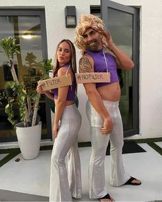 two women dressed in white pants and purple shirts are holding cardboard signs with words on them