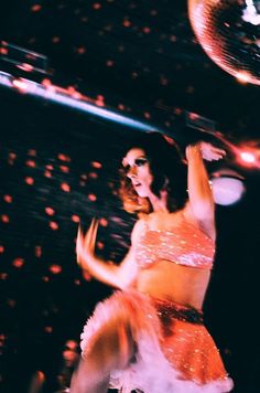 a woman in an orange dress dancing on stage with lights and disco balls behind her