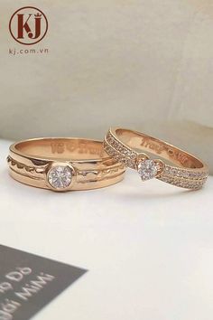 two gold wedding rings with diamonds on top of each other, sitting on a white surface