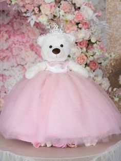 a white teddy bear wearing a pink dress with a tiara on it's head