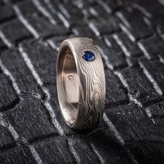 * Price may vary depending on ring size, please inquire with us directly with your needed size for accurate pricing! This Mokume Gane ring is shown in the Twist pattern and the Smoke metal combination. It also features a lovely blue sapphire, a low-dome profile, and an etched finish. The Smoke palette features 14k White Gold, Palladium and Sterling Silver.  Palette: Smoke Pattern: Twist Width Shown: 6mm Size Shown: 6.25 Finish: Satin Profile: Low Dome Stone: 3mm Blue Sapphire Setting: Flush  The price on this listing does NOT reflect all possible stone and setting fees. The price is specific to these stones and this setting style. Please inquire with us directly with your preferences for stone size and setting.  We care about customer service and would like to hear from you! Please contact Unique Stainless Steel Promise Ring, Modern Rings With Engraving Option, White Gold Etched Promise Ring, Hand Forged Engraved Promise Ring, Etched Round Promise Ring, Etched Promise Ring, Modern Etched Ring Jewelry, Modern Etched Jewelry For Anniversary, Modern Sterling Silver Rings With Engraving Option