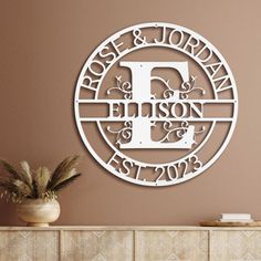 the monogrammed metal wall art is displayed in front of a brown wall with a potted plant