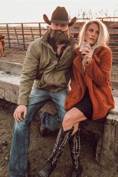 a man and woman sitting on a wooden bench in front of a fence with cows