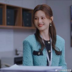 a young woman in a blue jacket smiles at the camera while standing next to a desk