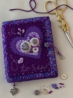 a pair of scissors sitting on top of a purple book next to buttons and thread