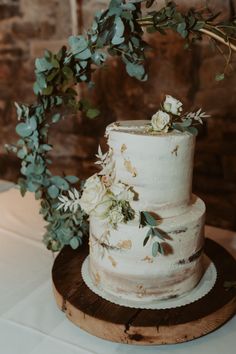 a white wedding cake with flowers and greenery on top sitting on a wooden plate