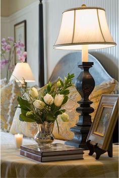 a lamp on a table next to a vase with flowers in it and two framed pictures