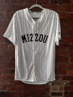 The Mizzou Retro Baseball Jersey is perfect unisex statement or layering piece. Lightweight and sweat-wicking material ensures maximum comfort and breathability. Full button front and unisex design pairs perfectly with any outfit. Western text detailing adds an elevated touch and class. Breathable Collegiate Tops For College, Casual White Baseball Jersey With Team Name, Casual White Baseball Jersey, White Casual Baseball Jersey For Game Day, Casual White Baseball Jersey For Game Day, White Cotton Sporty Baseball Jersey, Breathable Casual Baseball Jersey For Sports Season, Casual Cotton Baseball Jersey Breathable, Casual Short Sleeve Breathable Baseball Jersey