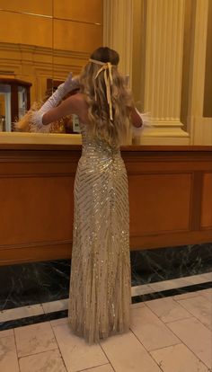 a woman standing in front of a counter wearing a long silver dress with sequins on it