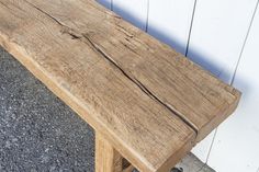 a wooden bench sitting on top of a sidewalk next to a white wall and cement floor