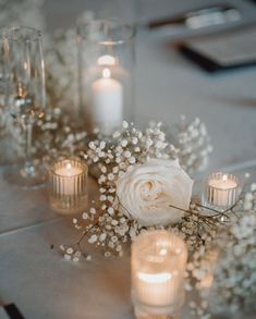 white flowers and candles on a table with glass vases filled with baby's breath