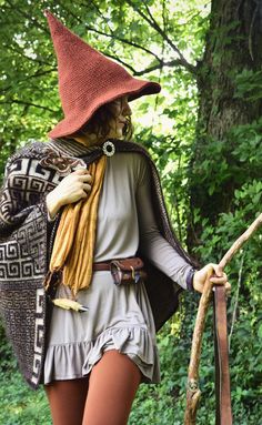 a woman in a costume and hat walking through the woods