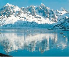 the mountains are covered in snow and there is still water on the lake below them