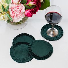 three green velvet coasters next to a glass of red wine