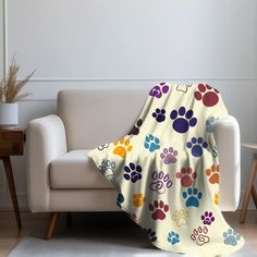 a dog paw print blanket sitting on top of a couch next to a white chair