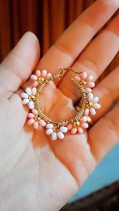 a hand holding a small gold and pink beaded hoop earring in it's palm