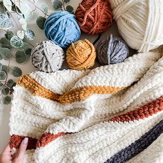 several balls of yarn are laid out on a white blanket with a person's hand