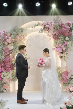 a bride and groom standing in front of a floral arch at the end of their wedding ceremony