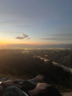 a person laying on top of a hill with the sun setting in the distance behind them