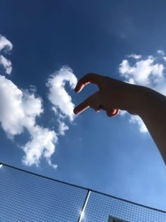 a person pointing at the sky with their hand in front of a tennis court net