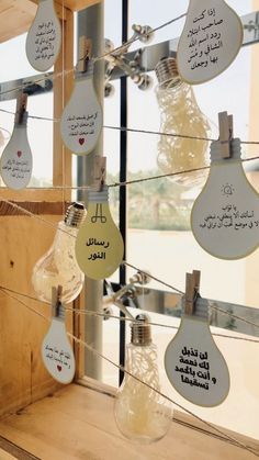 several light bulbs are hanging from wires with notes attached to them in arabic and english