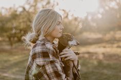 a woman holding a small dog in her arms and looking off into the distance with trees in the background