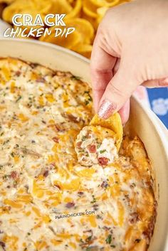 a hand dipping a tortilla chip into a casserole dish with cheese