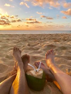 a person sitting in the sand with a coconut drink