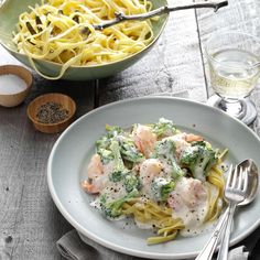 pasta with shrimp, broccoli and sauce in a bowl next to a glass of water