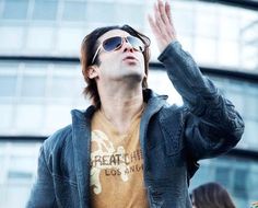 a man wearing sunglasses is standing in front of a building with his hand up to the sky