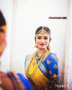 a woman in a blue and yellow sari is looking at her reflection on the mirror