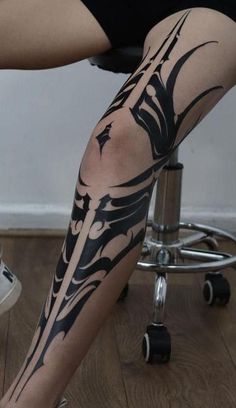 a woman sitting on top of a chair with her leg covered in black and white tattoos